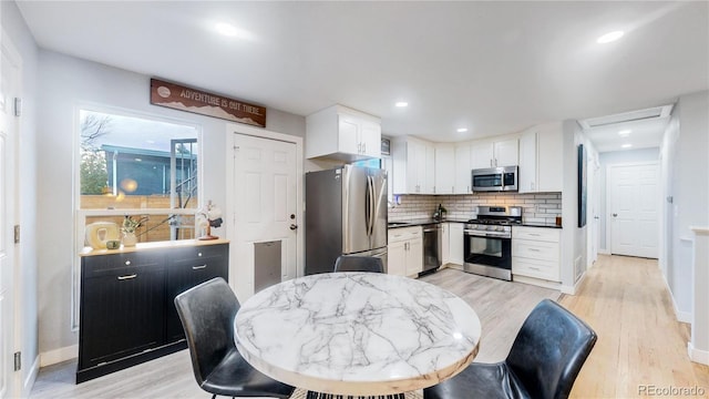 kitchen featuring tasteful backsplash, white cabinets, light hardwood / wood-style floors, and appliances with stainless steel finishes