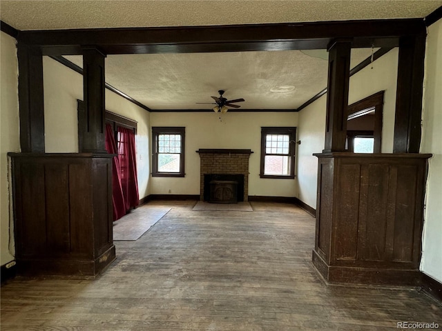 unfurnished living room featuring ceiling fan, a textured ceiling, hardwood / wood-style flooring, and a brick fireplace