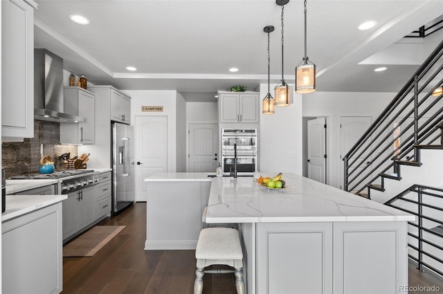 kitchen with a kitchen island with sink, dark wood-type flooring, appliances with stainless steel finishes, and wall chimney exhaust hood