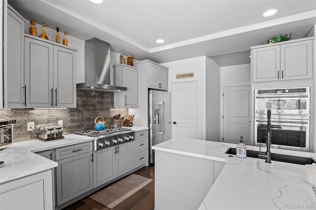 kitchen with light stone counters, backsplash, appliances with stainless steel finishes, wall chimney range hood, and dark wood-style flooring