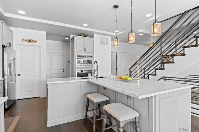 kitchen featuring dark wood-style floors, visible vents, a sink, stainless steel appliances, and a kitchen breakfast bar