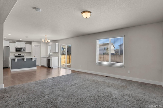 unfurnished living room featuring carpet, a textured ceiling, and an inviting chandelier