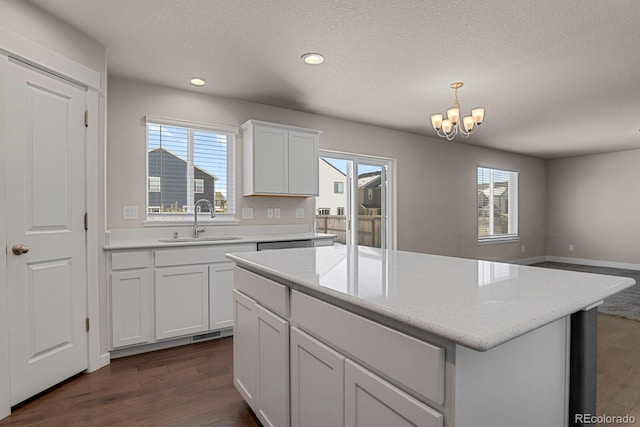 kitchen featuring dark wood-type flooring, an inviting chandelier, white cabinets, sink, and a kitchen island