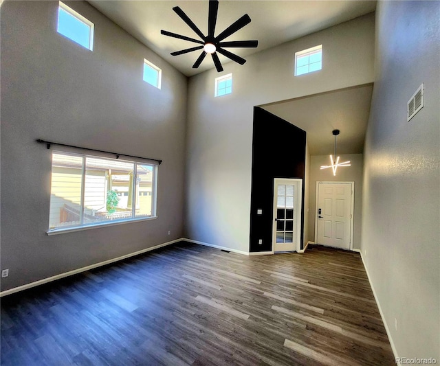 empty room featuring visible vents, baseboards, ceiling fan, dark wood finished floors, and a towering ceiling