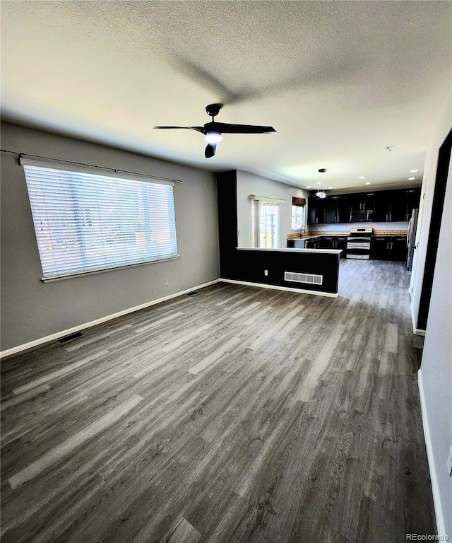 unfurnished living room featuring visible vents, dark wood-type flooring, a ceiling fan, a textured ceiling, and baseboards