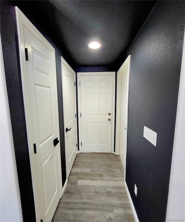 hall with light wood finished floors, a textured ceiling, baseboards, and a textured wall