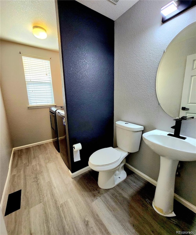 half bathroom featuring baseboards, separate washer and dryer, wood finished floors, and toilet