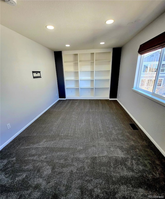 spare room with visible vents, a textured ceiling, baseboards, and dark colored carpet