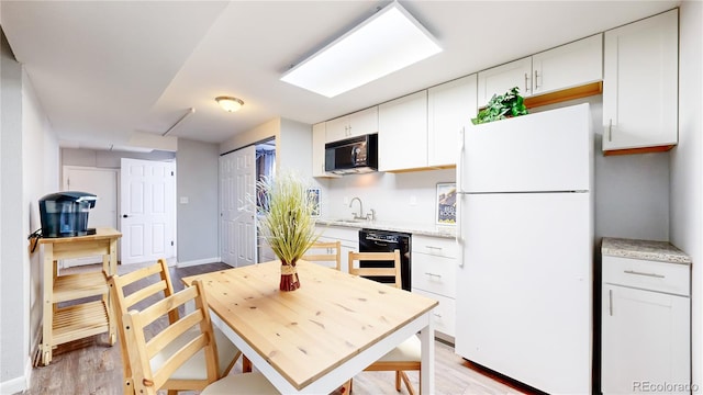 kitchen with sink, black appliances, white cabinetry, and light hardwood / wood-style flooring