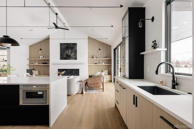 kitchen featuring stainless steel oven, light hardwood / wood-style floors, sink, and a wealth of natural light