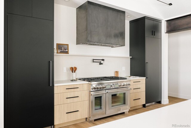 kitchen featuring light brown cabinetry, light hardwood / wood-style floors, wall chimney exhaust hood, and high quality appliances