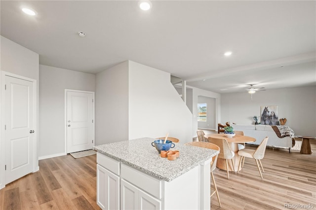 kitchen with ceiling fan, a center island, light stone counters, light hardwood / wood-style flooring, and white cabinets