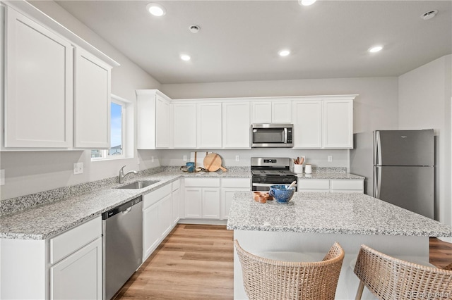 kitchen featuring sink, stainless steel appliances, a kitchen breakfast bar, light hardwood / wood-style floors, and white cabinets