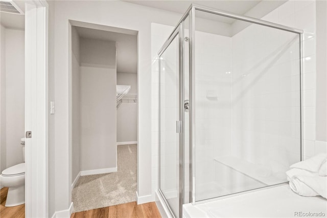 bathroom with hardwood / wood-style floors, a shower with door, and toilet