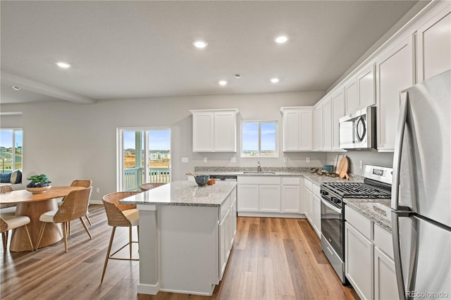 kitchen with a center island, white cabinets, light wood-type flooring, light stone countertops, and appliances with stainless steel finishes