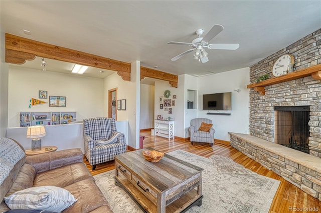 living room with ceiling fan, beam ceiling, a large fireplace, and hardwood / wood-style flooring