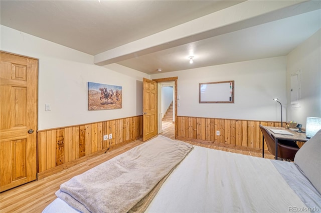 bedroom with beam ceiling, light wood-type flooring, and wood walls