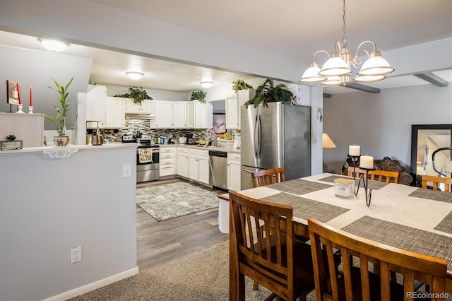 kitchen with hardwood / wood-style floors, tasteful backsplash, a chandelier, hanging light fixtures, and appliances with stainless steel finishes