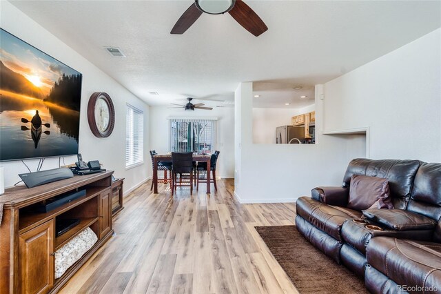 living room with baseboards, visible vents, ceiling fan, and light wood finished floors