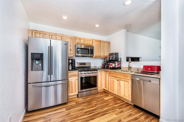 kitchen with stainless steel appliances, light brown cabinetry, a sink, and light stone countertops