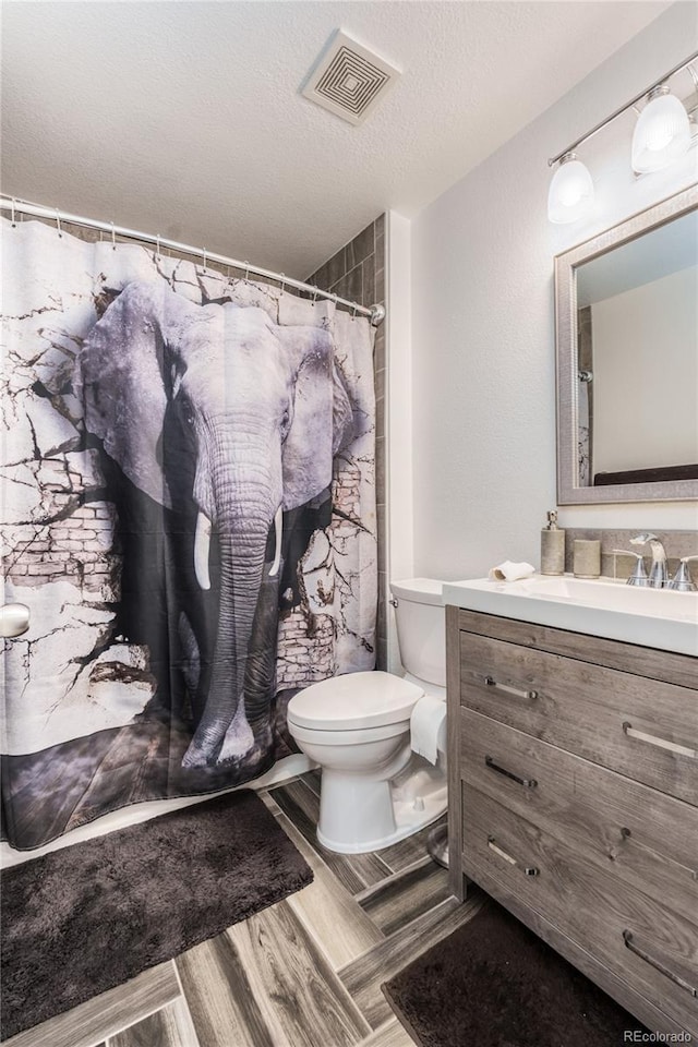 bathroom with visible vents, toilet, wood finished floors, a textured ceiling, and vanity