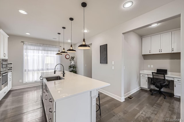 kitchen featuring pendant lighting, sink, white cabinets, dark hardwood / wood-style flooring, and a kitchen island with sink