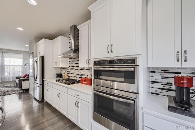 kitchen featuring white cabinetry, wall chimney range hood, decorative backsplash, and appliances with stainless steel finishes