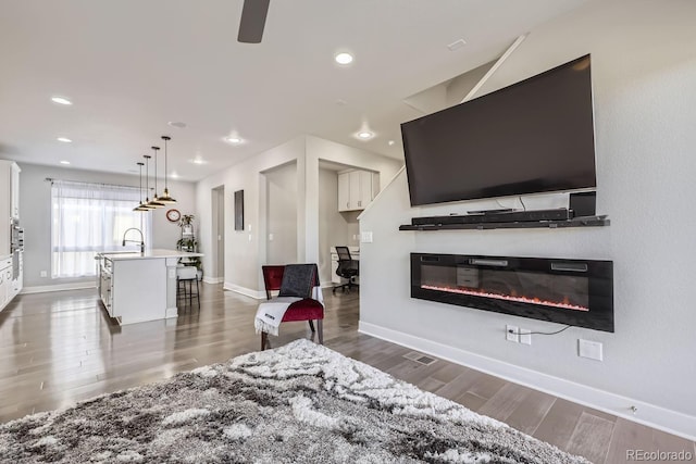 living room with a glass covered fireplace, recessed lighting, baseboards, and wood finished floors