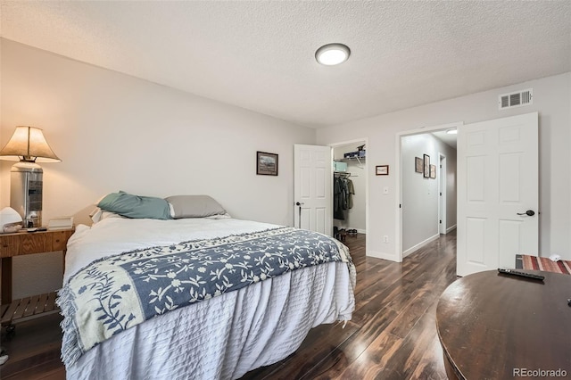 bedroom featuring dark wood-type flooring, a closet, a walk in closet, and a textured ceiling