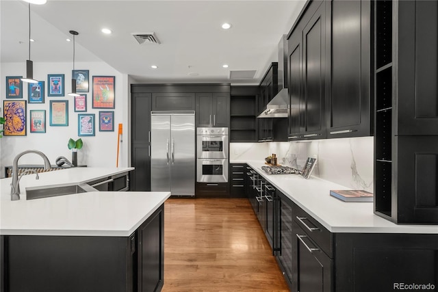 kitchen featuring appliances with stainless steel finishes, sink, backsplash, hanging light fixtures, and light wood-type flooring