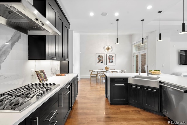 kitchen with pendant lighting, appliances with stainless steel finishes, wall chimney exhaust hood, light hardwood / wood-style floors, and sink