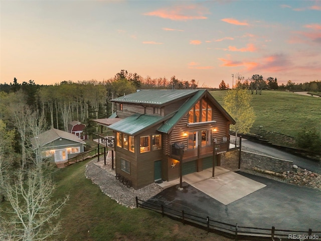 11690 Rampart Range Rd, Woodland Park, CO 80863 - back of property at dusk with driveway, an attached garage, metal roof, a balcony, and log siding
