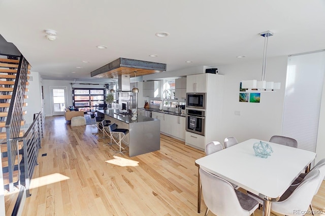 kitchen with white cabinetry, light hardwood / wood-style flooring, ventilation hood, a breakfast bar area, and appliances with stainless steel finishes