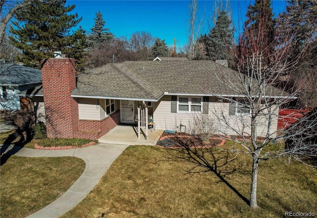 view of front of house featuring a front lawn, roof with shingles, a chimney, and brick siding