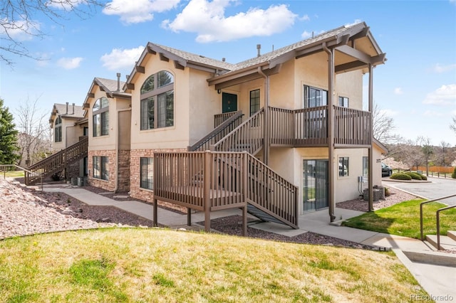 2172 Denton Grv Unit 203, Colorado Springs, CO 80919 - back of property featuring stone siding, stucco siding, a lawn, central air condition unit, and stairway