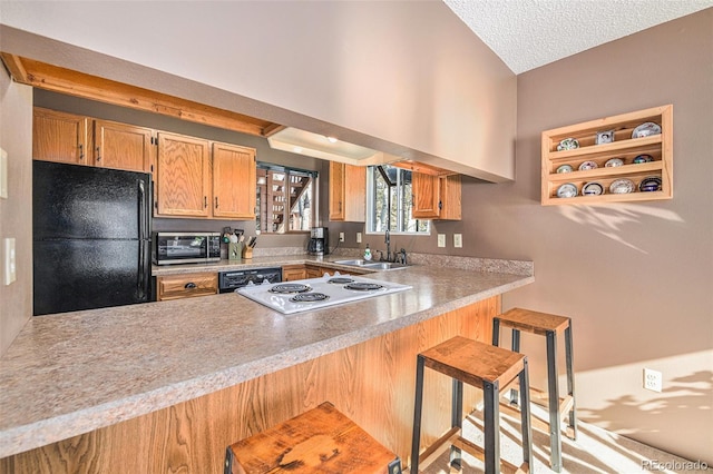 kitchen featuring sink, black appliances, a textured ceiling, a kitchen bar, and kitchen peninsula