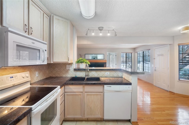 kitchen featuring sink, backsplash, kitchen peninsula, light brown cabinets, and white appliances