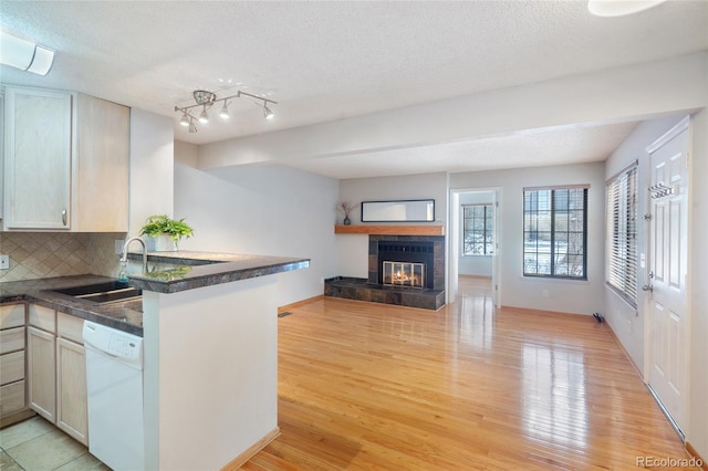 kitchen with kitchen peninsula, sink, backsplash, light hardwood / wood-style floors, and white dishwasher