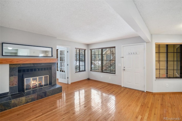 unfurnished living room featuring hardwood / wood-style flooring, a tile fireplace, and a textured ceiling