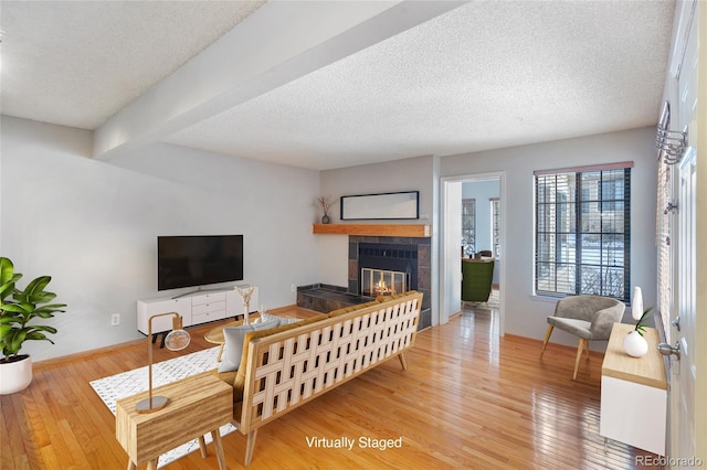 living room featuring hardwood / wood-style flooring, a tiled fireplace, a textured ceiling, and beamed ceiling