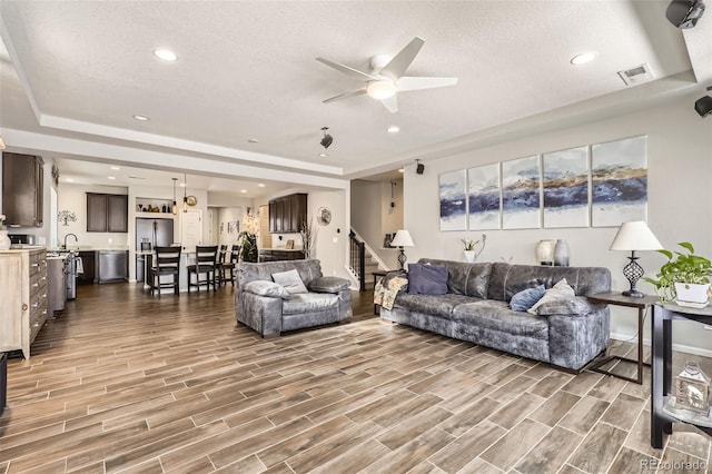 living room with ceiling fan, sink, a raised ceiling, a textured ceiling, and hardwood / wood-style flooring