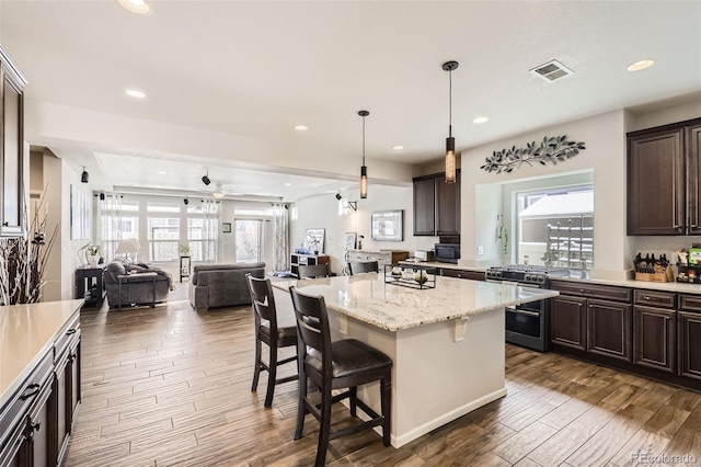 kitchen featuring dark brown cabinetry, a center island, hanging light fixtures, a breakfast bar, and high end stainless steel range