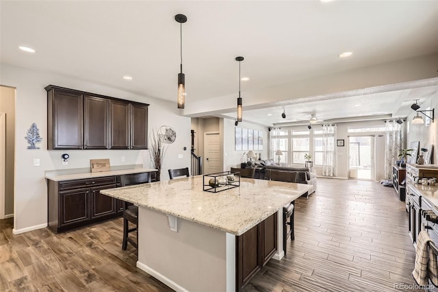 kitchen featuring ceiling fan, a kitchen island, a kitchen bar, and dark brown cabinetry