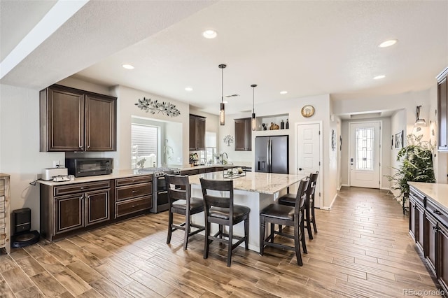 kitchen with light stone countertops, a center island, stainless steel appliances, decorative light fixtures, and a breakfast bar