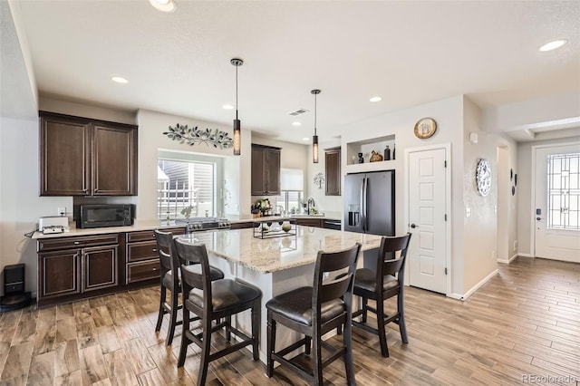 kitchen with stainless steel refrigerator with ice dispenser, a kitchen breakfast bar, a center island, light hardwood / wood-style floors, and hanging light fixtures