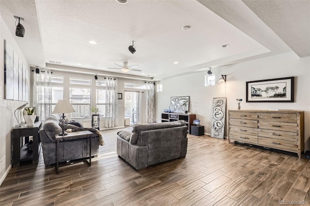 living room with ceiling fan, a raised ceiling, and a textured ceiling