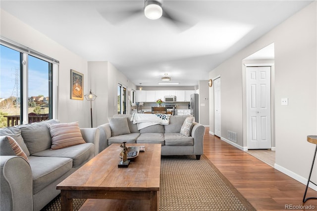 living room featuring ceiling fan, light wood-style floors, healthy amount of natural light, and baseboards