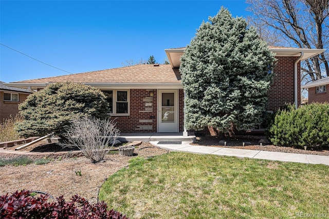 view of front facade with brick siding, a front lawn, and a shingled roof