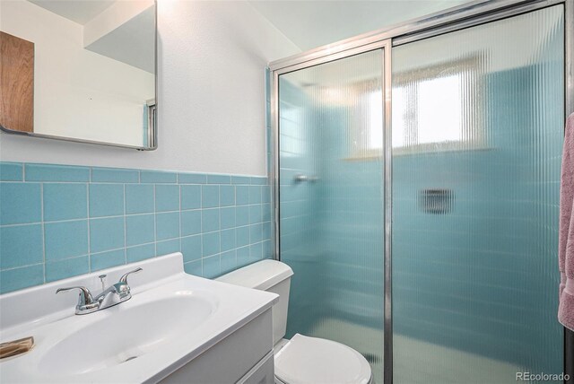 bathroom featuring tile walls, a shower stall, toilet, vanity, and wainscoting