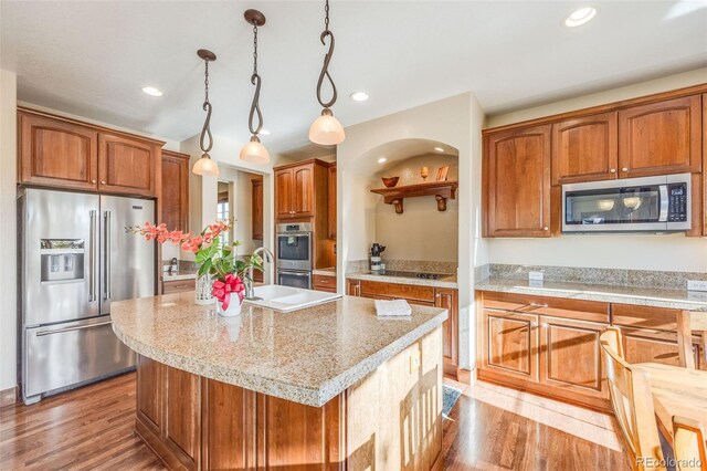 kitchen featuring pendant lighting, light stone countertops, a kitchen island with sink, stainless steel appliances, and light wood-type flooring